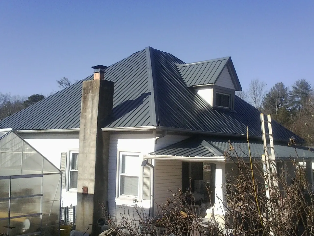 Dark blue standing seam metal roof on a white farmhouse with dormer — Slate & Tile Roof Repair by Roofing Brothers in Seville