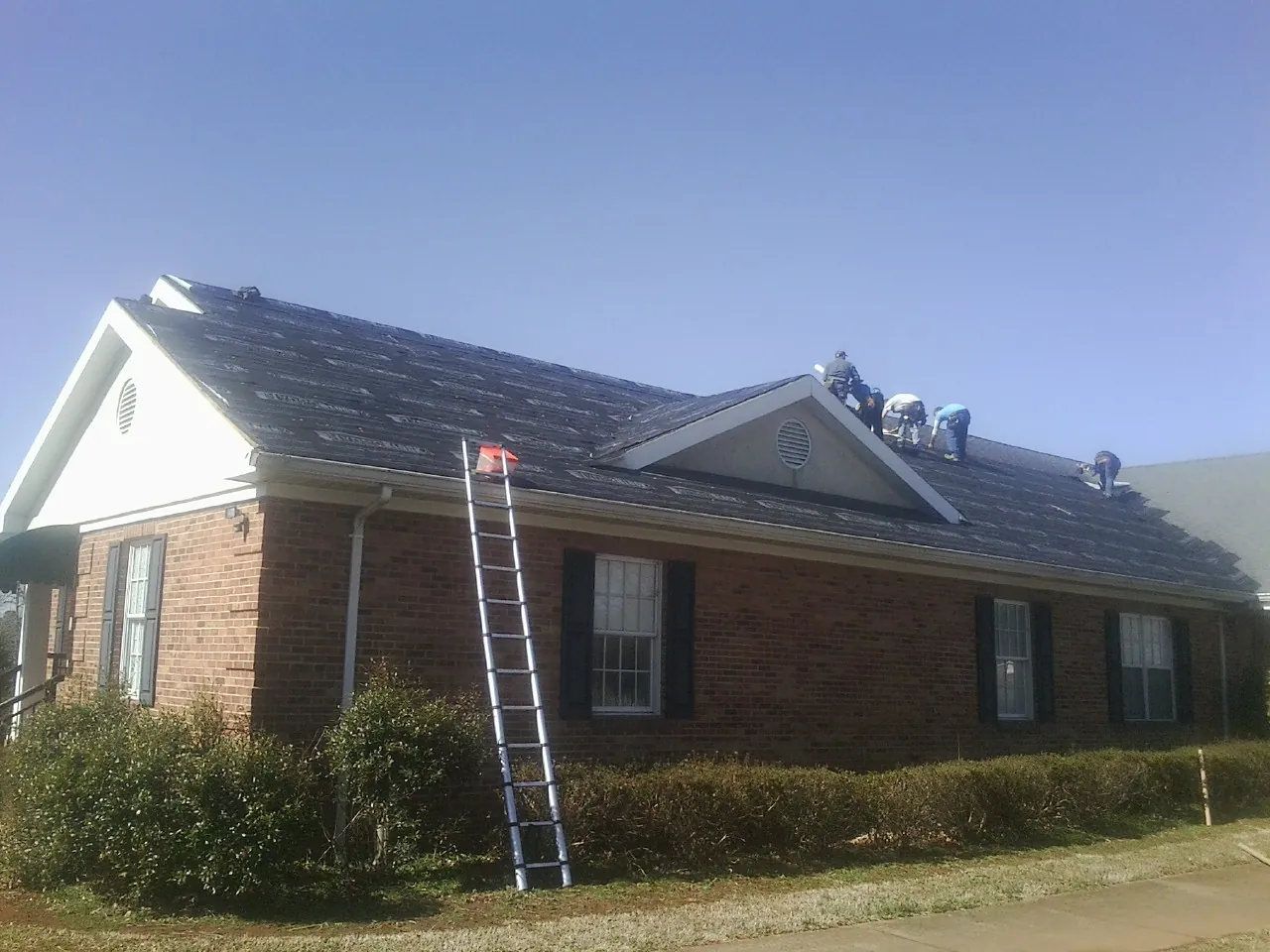 Crew tearing shingles off a brick ranch roof with a ladder set — Metal Roof Repair work by our crew in Seville
