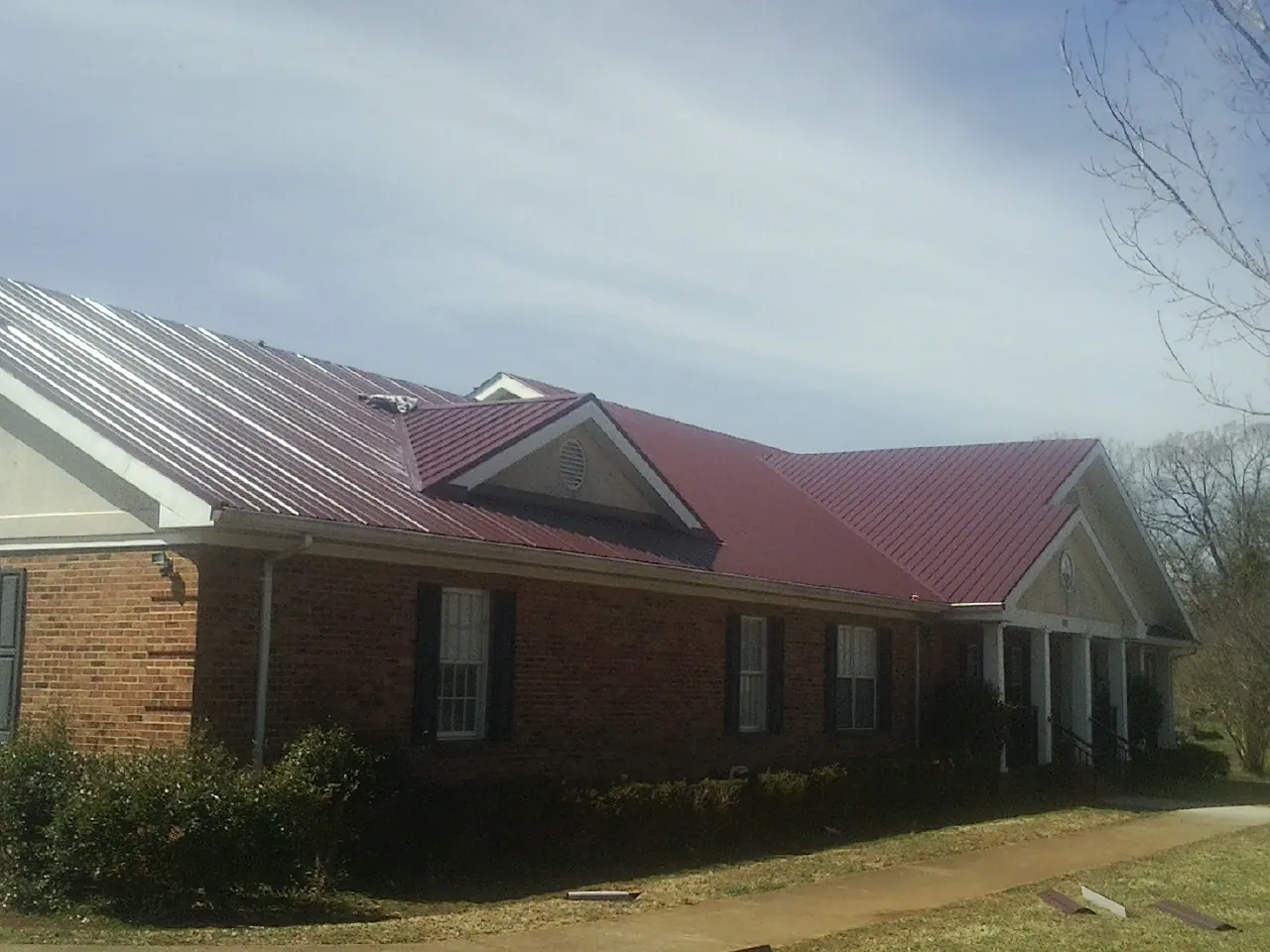 Red metal roof with gabled entries on a long brick building, from a Hail Damage Roof Repair job in Seville