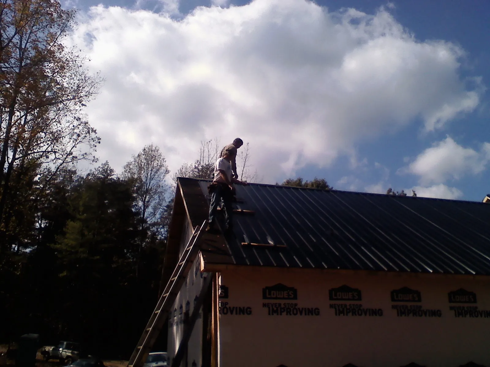 Roofer fastening dark metal panels high against a cloudy sky, from a Roof Inspection job in Seville